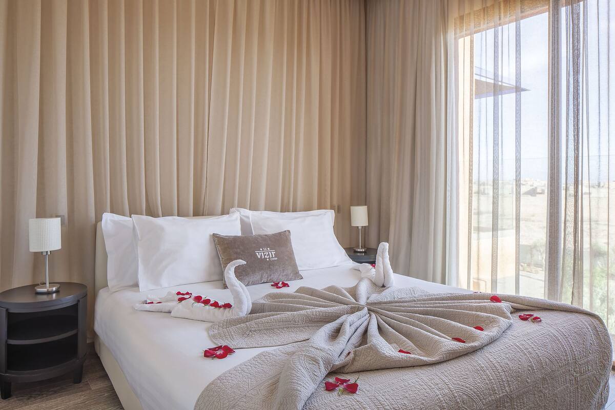 A neatly made bed with a swan-shaped towel arrangement, a pillow with a logo, and a bedside lamp.