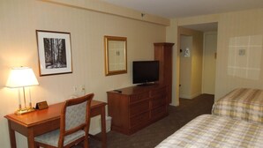 Een hotelkamer met een bed, een bureau met stoel, een televisie, een dressoir en een fotokader aan de muur.