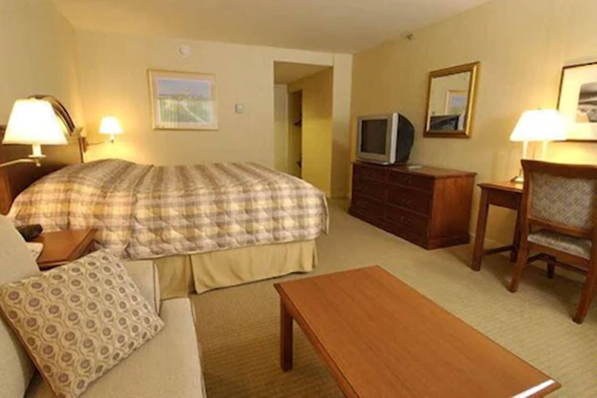 Ein Hotelzimmer mit einem Bett, einem Fernseher, einem Schreibtisch, einem Sessel und einer Lampe.