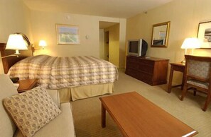 A hotel room with a bed, a television, a desk, a chair, and a lamp. - Rockville Centre Inn (Lynbrook)
