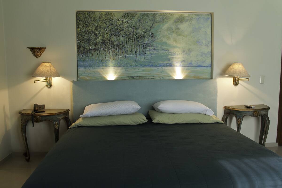 A bedroom with a bed, two bedside tables, two wall-mounted lamps, and a painting above the bed.