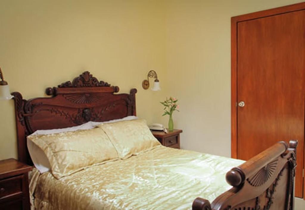 A bedroom with a wooden bed, a nightstand, a bedside lamp, and a door.