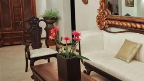 A living room with a wooden cabinet, a sofa, a coffee table with flowers, and a mirror with an ornate frame. - Casa Madonna La Providence Hotel Boutique (Guadalajara)
