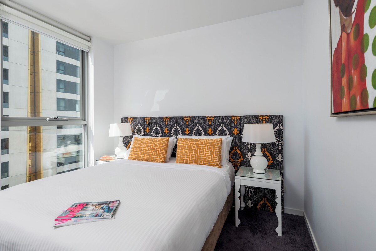A neatly made bed with patterned pillows, a bedside table with a lamp, and a framed artwork on the wall.