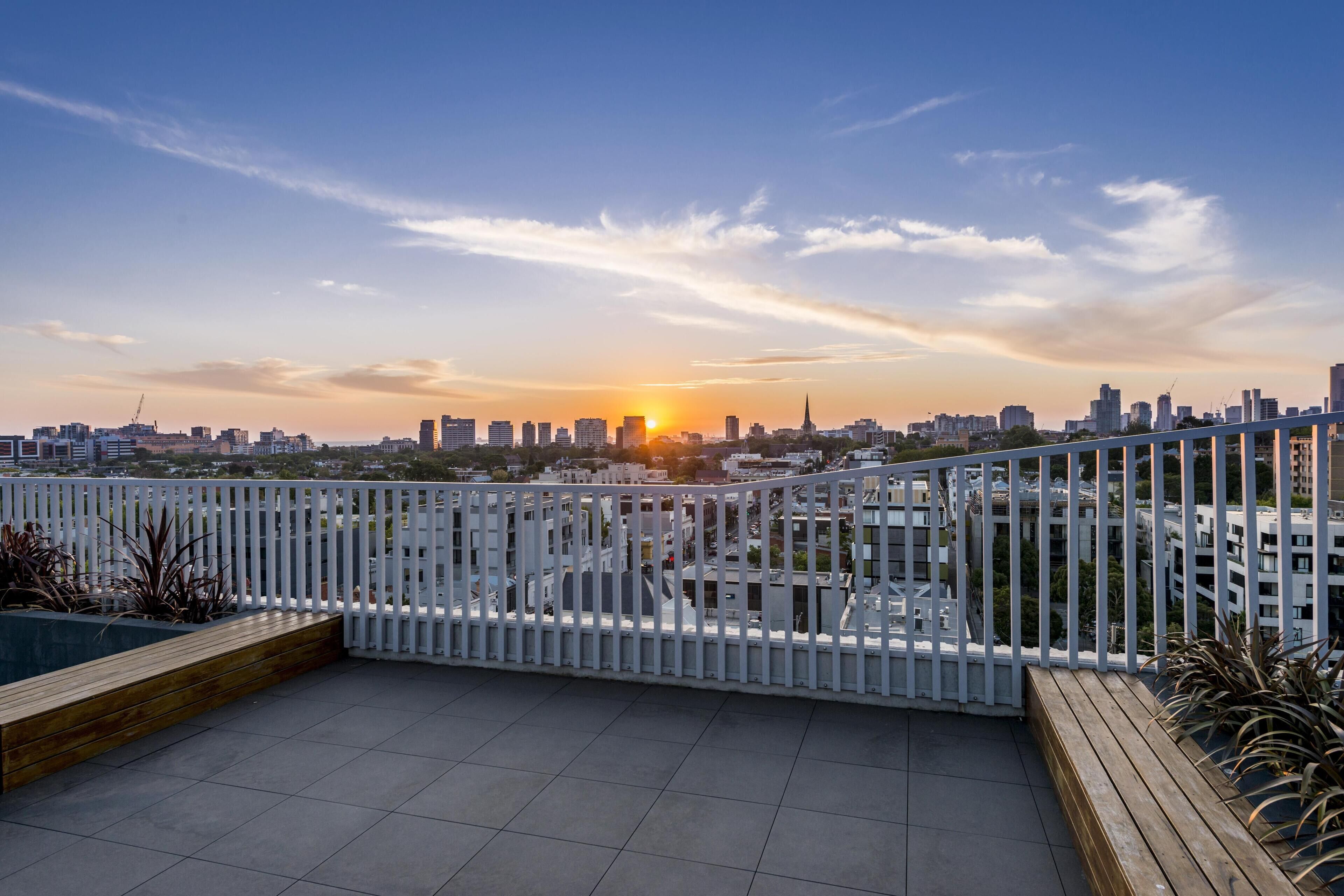 A rooftop terrace with a city skyline view, white railing, and tiled floor.