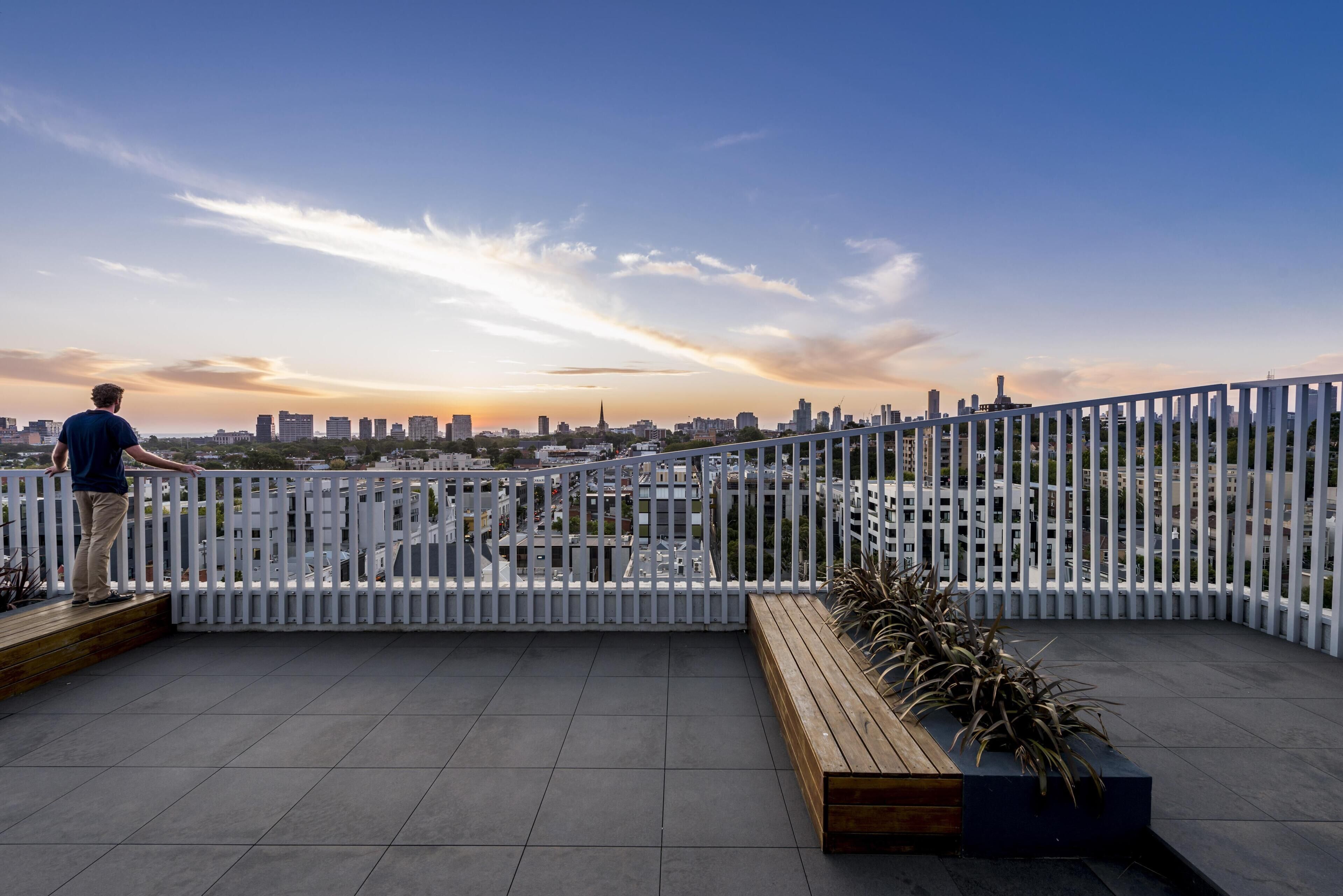 A person standing on a rooftop terrace with a city skyline in the background.
