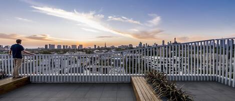A person standing on a rooftop terrace with a city skyline in the background.