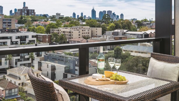 Un balcón con mesa lista para una comida, una botella de vino y vistas a la ciudad.