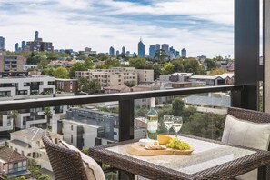 A balcony with a table set for a meal, a bottle of wine, and a cityscape view. - Oaks Melbourne South Yarra Suites (South Yarra)