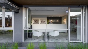 Una recepción de hotel moderna con puertas de vidrio, un mostrador de recepción y dos sillas blancas afuera.