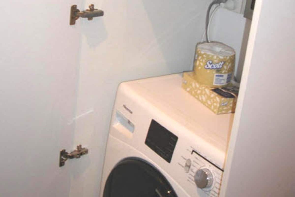 A compact laundry room with a front-loading washing machine, a dryer, and a small shelf with a can of Scott toilet paper.