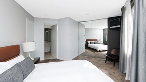 Een hotelkamer met een groot bed, nachtkastje met lamp, spiegel, stoel en televisie.