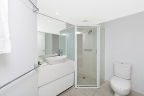 Un baño moderno con ducha de vidrio, lavamanos blanco y un inodoro.