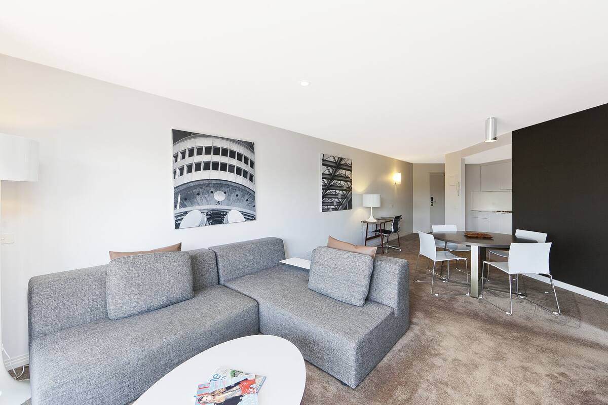 Un salon moderne avec un canapé d’angle gris, une table basse blanche et un coin repas comprenant une petite table et des chaises.