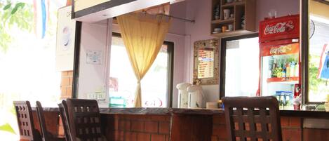 A café with a sign reading "Chá da Café," featuring a brick counter and wooden chairs.