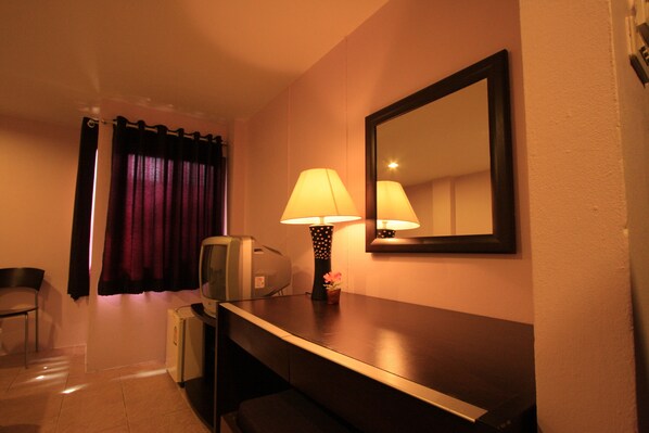 Une chambre d’hôtel équipée d’un bureau, d’une lampe, d’un miroir, d’une chaise et d’une petite table agrémentée d’une fleur.