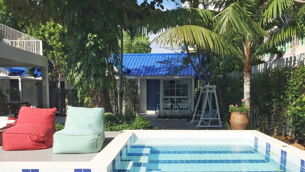 Una piscina con bordes de azulejos azules, rodeada de follaje y una valla blanca.