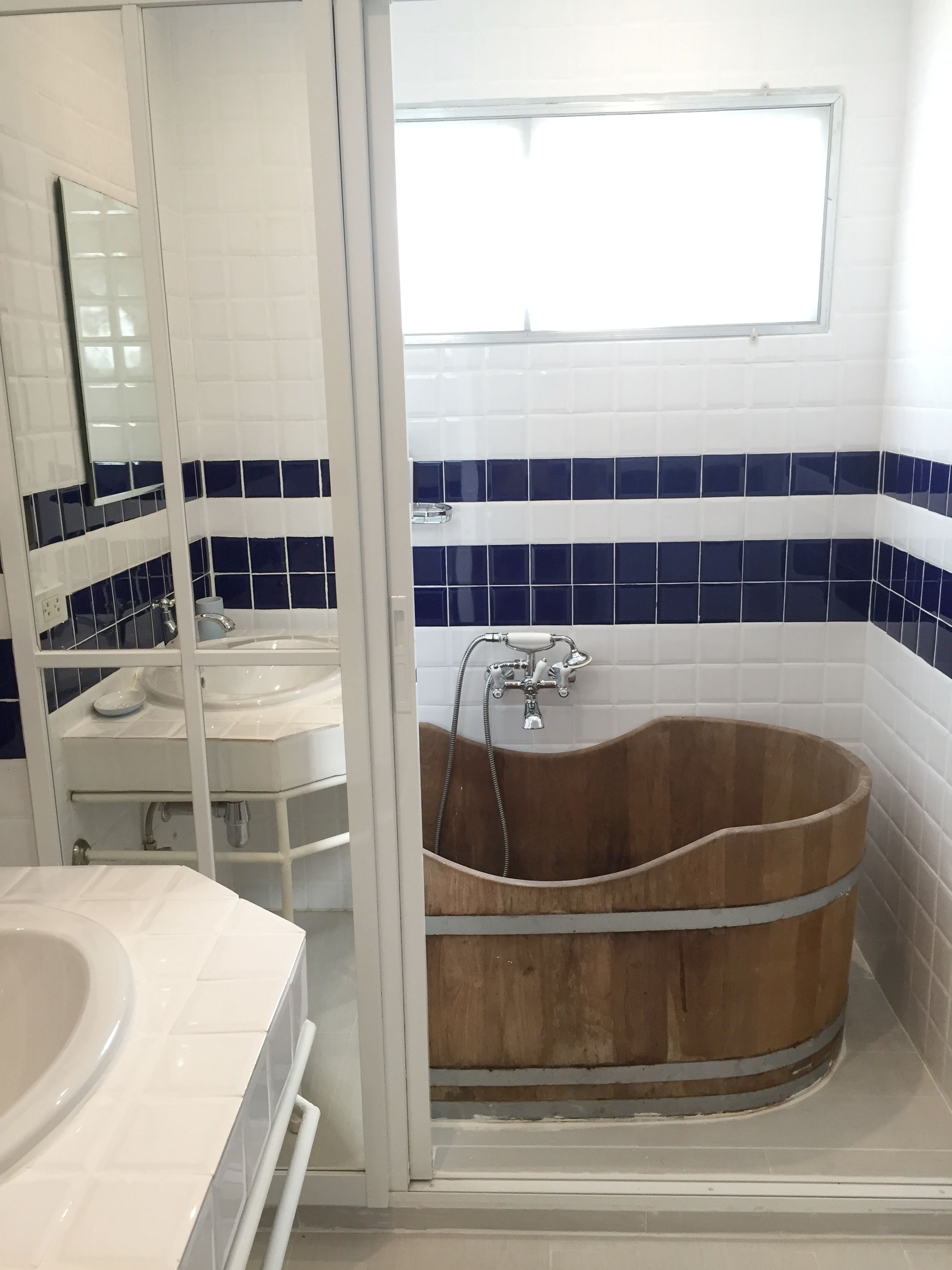 A bathroom with a wooden bathtub, white and blue tiled walls, a white sink, and a mirror.