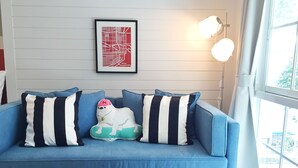 Un sofá azul con almohadones a rayas, un mapa enmarcado en la pared y una lámpara.
