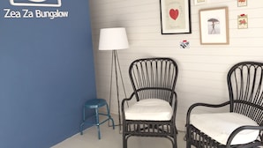 Una habitación con una pared azul de acento, dos sillas de mimbre negro con cojines blancos, un taburete azul pequeño, una lámpara de pie y varias imágenes y adornos enmarcados en la pared.