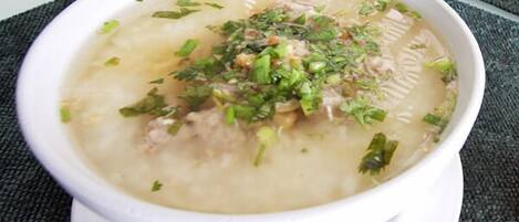 Un tazón de sopa con carne y hierbas verdes, servido en un tazón blanco sobre una mesa.
