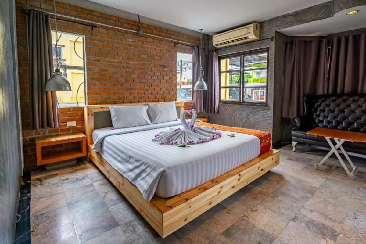 A modern bedroom with a brick wall, a wooden bed frame, a small table, and a black leather sofa.