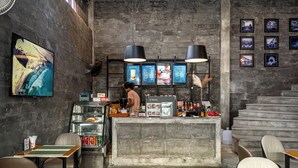Una cafetería con una pared de ladrillo rústico, una barra con carteles de menú, y una persona preparando comida.