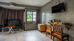 Una habitación moderna con sofá, una mesita, televisor montado en la pared y una ventana con cortinas.