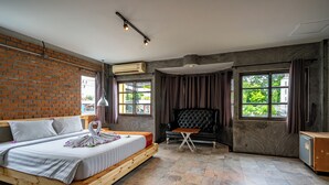Una habitación de hotel moderna con pared de ladrillo, una cama grande, un rincón de estar y ventanas amplias.