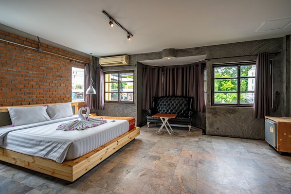 A modern hotel room with a brick wall, a large bed, a seating area, and large windows.