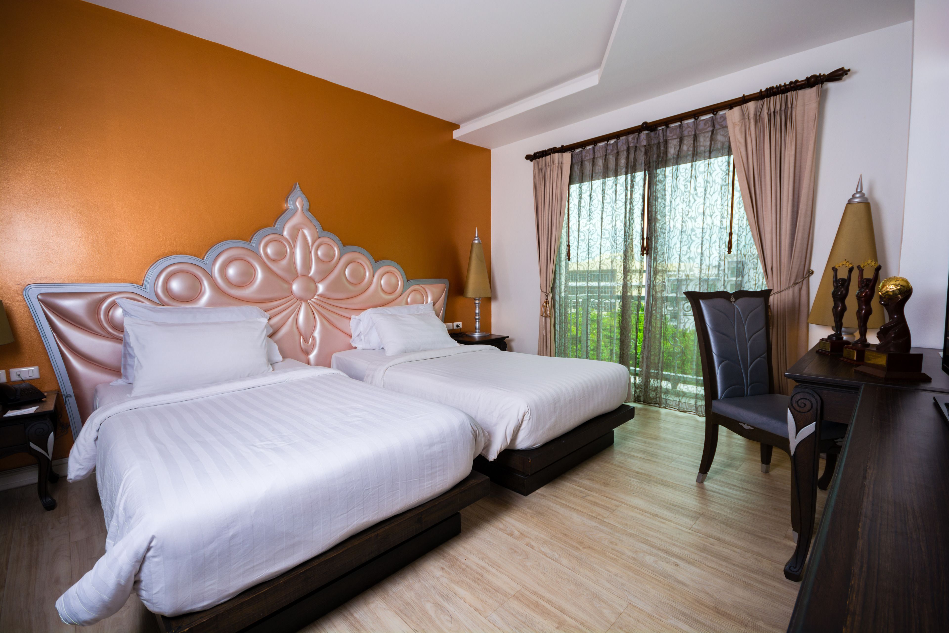 A hotel room with two beds, a chair, a desk, and a window with curtains.