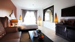 A hotel room with a bed, a sofa, a dining table with fruit, a TV, and a decorative cabinet. - Chillax Resort (Bangkok)