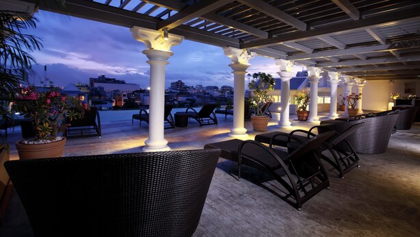 An outdoor seating area with white columns, wicker furniture, and potted plants. - Chillax Resort (Bangkok)