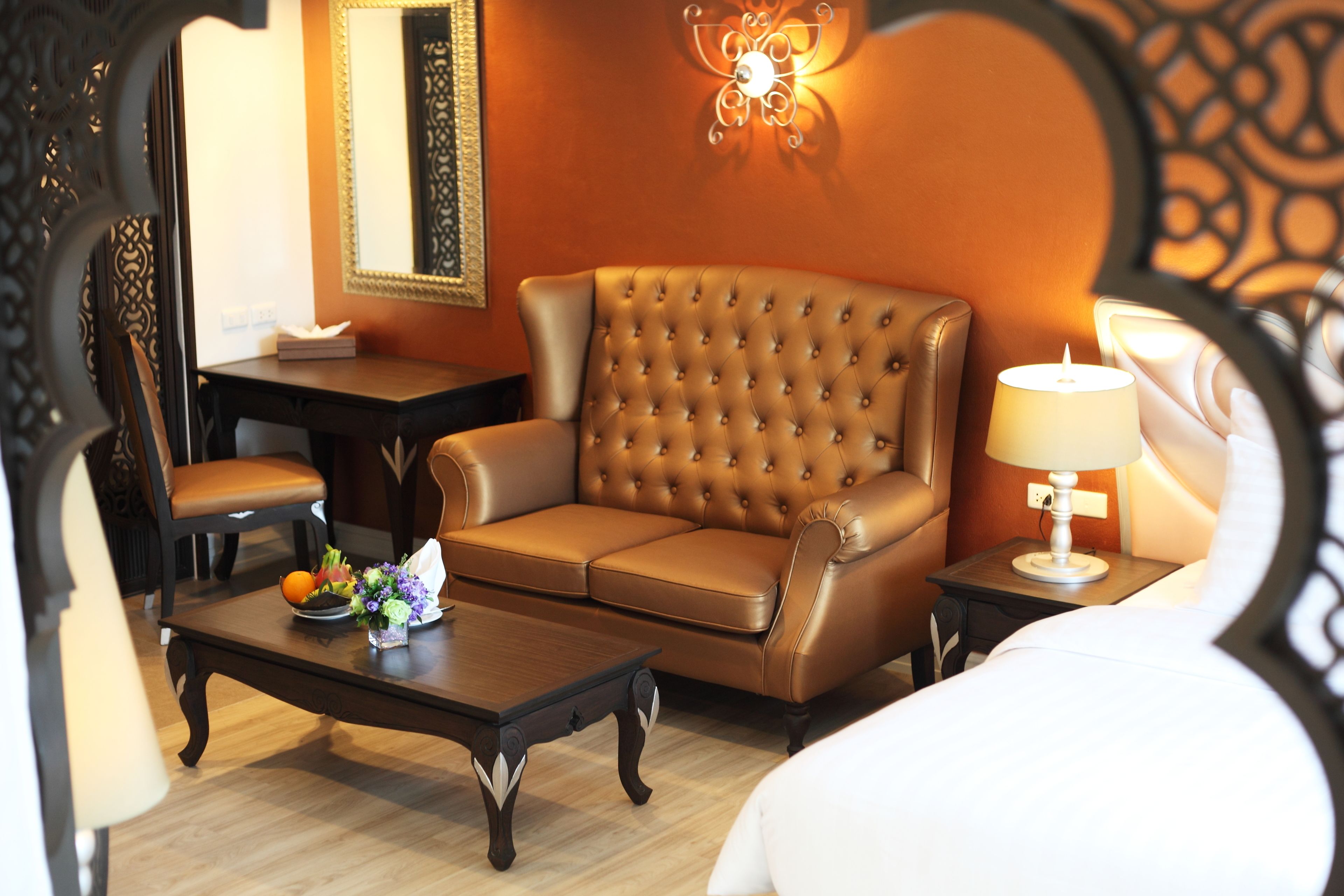 Une chambre d’hôtel avec un canapé en cuir marron, une table basse en bois sur laquelle se trouve un panier de fruits, un bureau avec une chaise et une table de chevet avec une lampe.