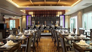 A restaurant with a patterned floor, multiple dining tables set with white tablecloths, and a modern ceiling design. - Chillax Resort (Bangkok)