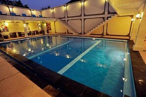 Una piscina con una línea de agua azul cristalina, contigua a un edificio de fachada blanca y una escalera que conduce a un nivel superior.