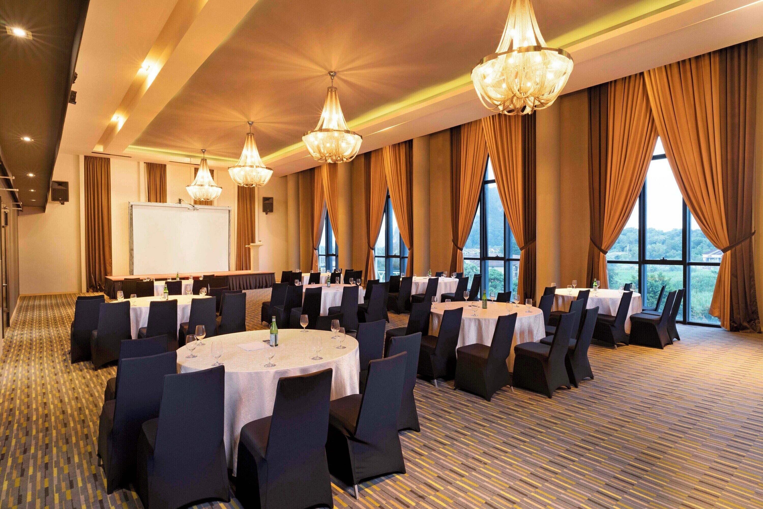 A conference room with round tables, black chairs, and large windows with curtains.