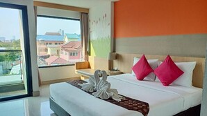 A hotel room with a bed, a nightstand, a lamp, and a view of buildings through a large window. - Memo Suite Pattaya (Pattaya)