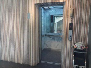 An elevator with a marble interior and a small shelf with flowers. - Memo Suite Pattaya (Pattaya)