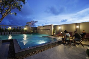 An outdoor swimming pool with a stone border, surrounded by seating areas and a low wall.