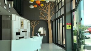 A modern reception area with a white reception desk, a large tree mural, and a view of the street outside. - Memo Suite Pattaya (Pattaya)