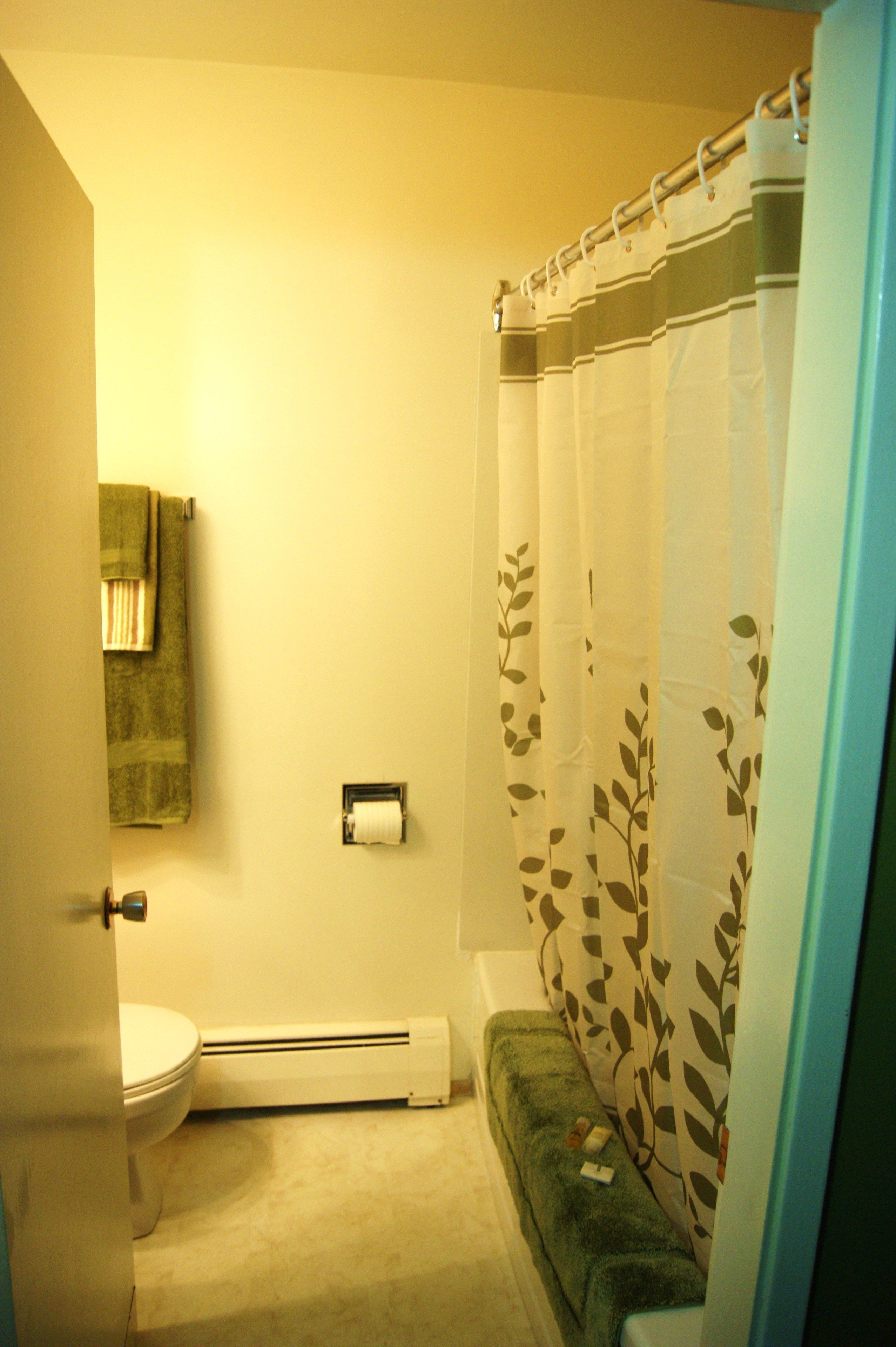 A bathroom with a toilet, a towel rack, a heater, and a shower curtain.