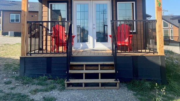 Una cabaña de madera con un porche, dos sillas Adirondack rojas y una escalera que lleva a la entrada.