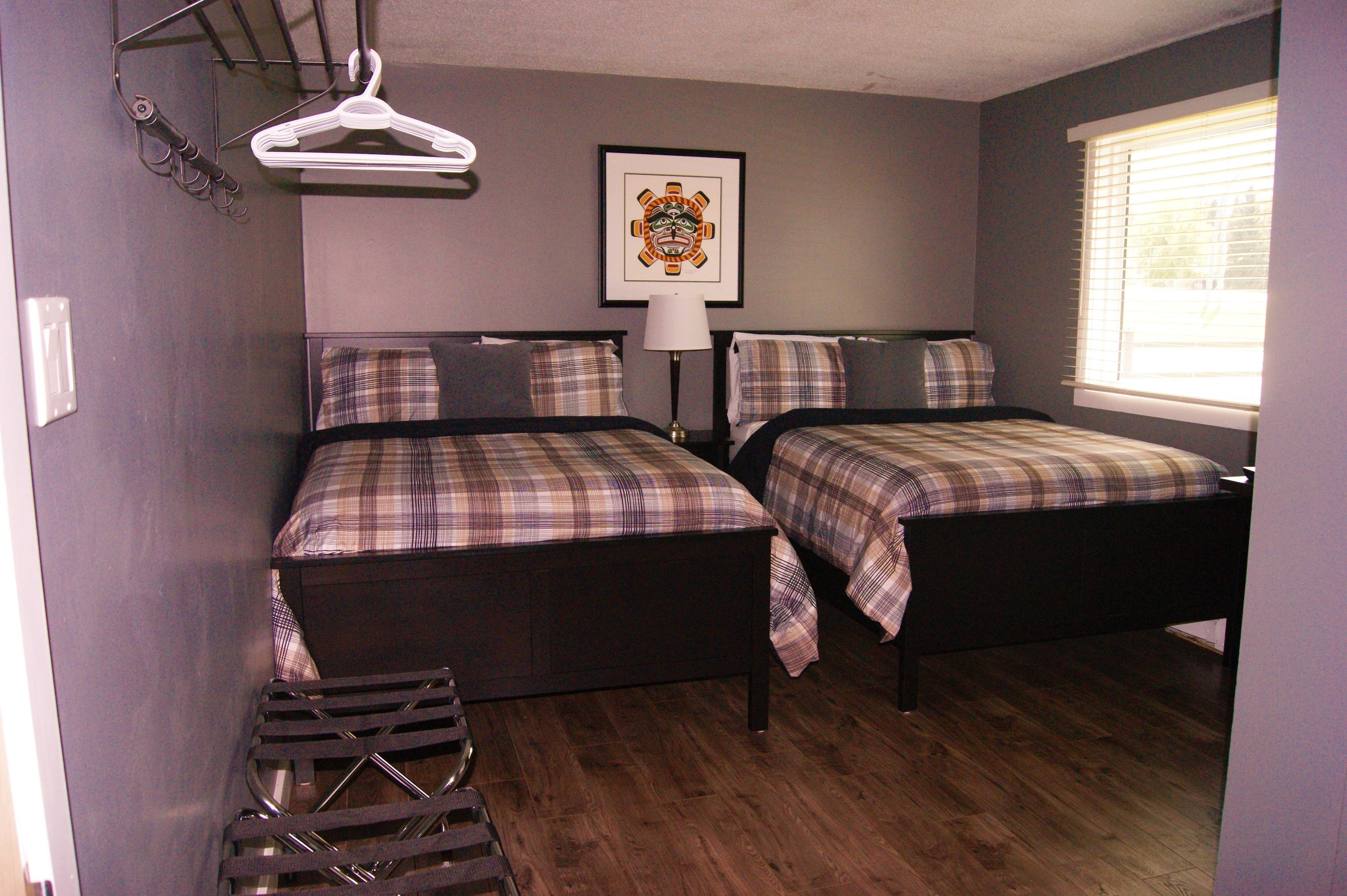 A bedroom with two beds, a hanging clothes rack, a framed picture on the wall, and a window with blinds.