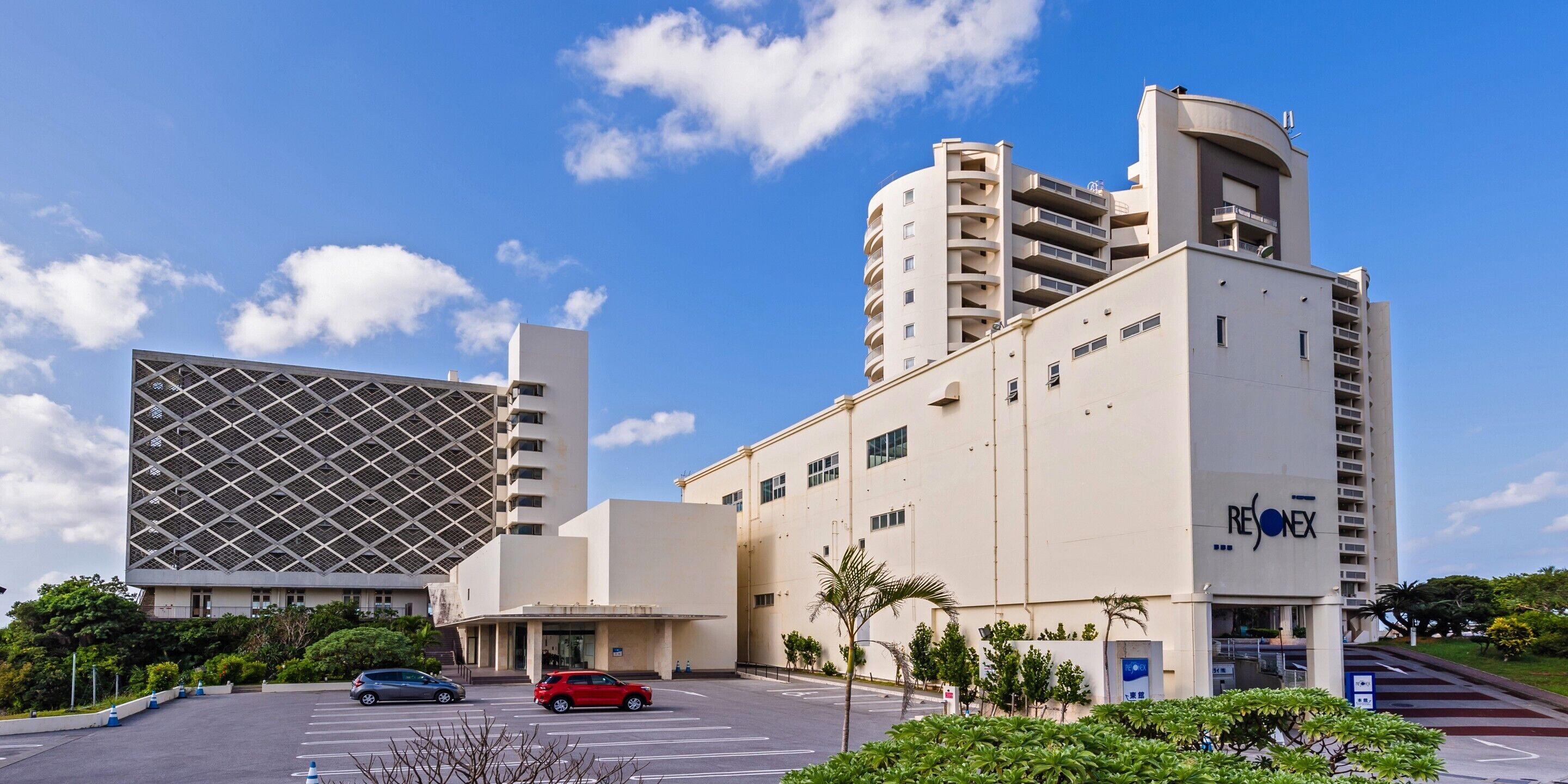 A modern building with a prominent entrance, a parking lot, and a clear blue sky.