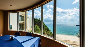 Una habitación con un ventanal que da a la playa, una mesa con mantel azul y una silla.
