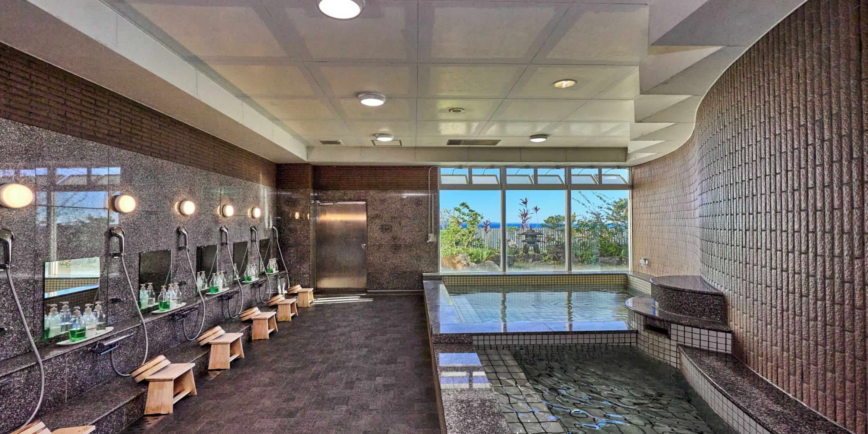 Ein modernes Badezimmer mit mehreren Waschbecken, einem großen Fenster und einem Whirlpoolbereich.