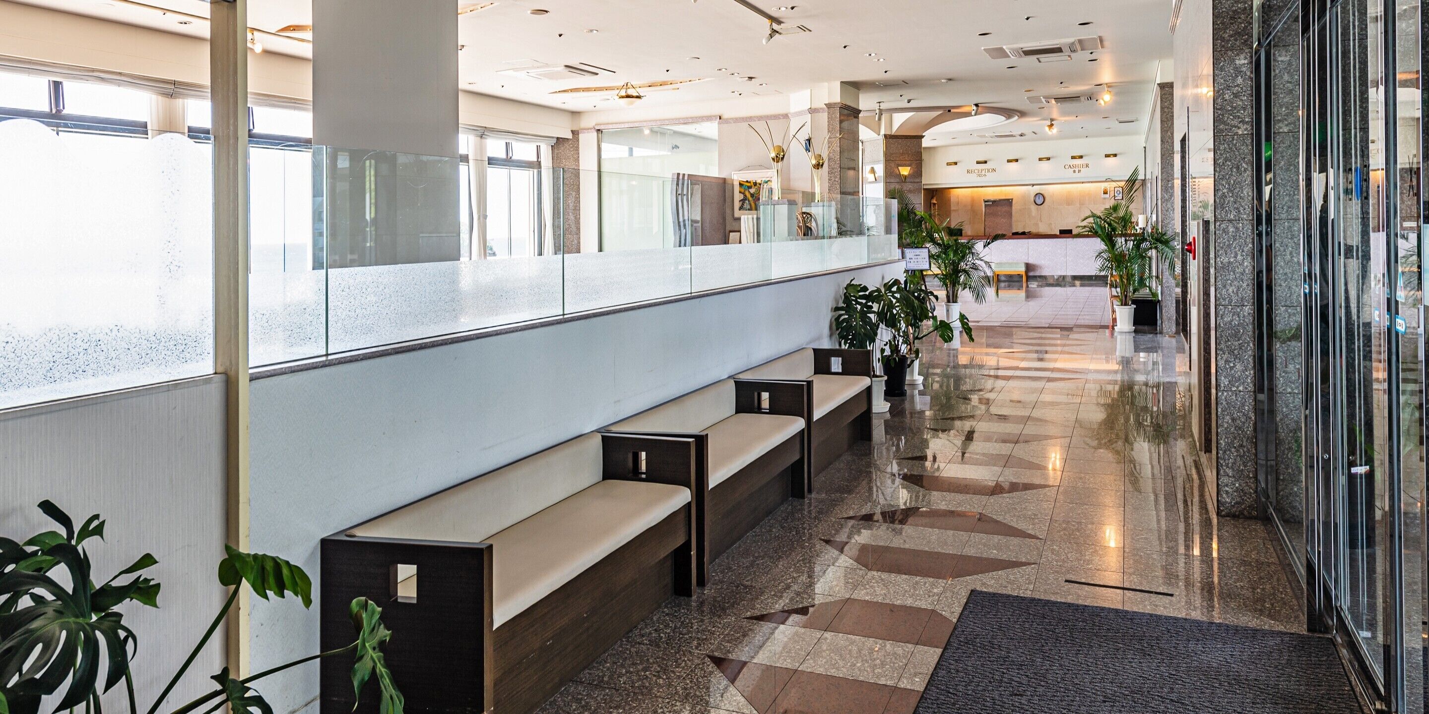 Een moderne hotel lobby met een receptiebalie, een zithoek en potplanten.