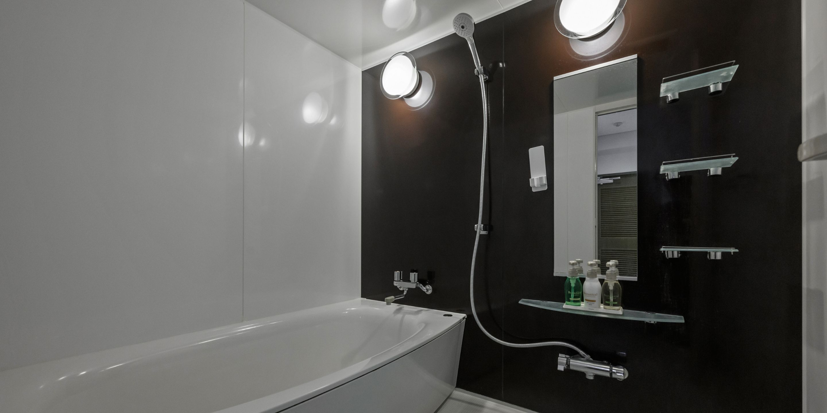 Ein modernes Badezimmer mit einer weißen Badewanne, einer Duschkabine aus Glas und einem Spiegel mit Ablagefläche darüber.