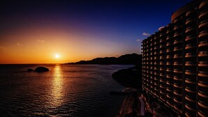 Un hotel moderno de gran altura con varios balcones que dan a una masa de agua al atardecer.